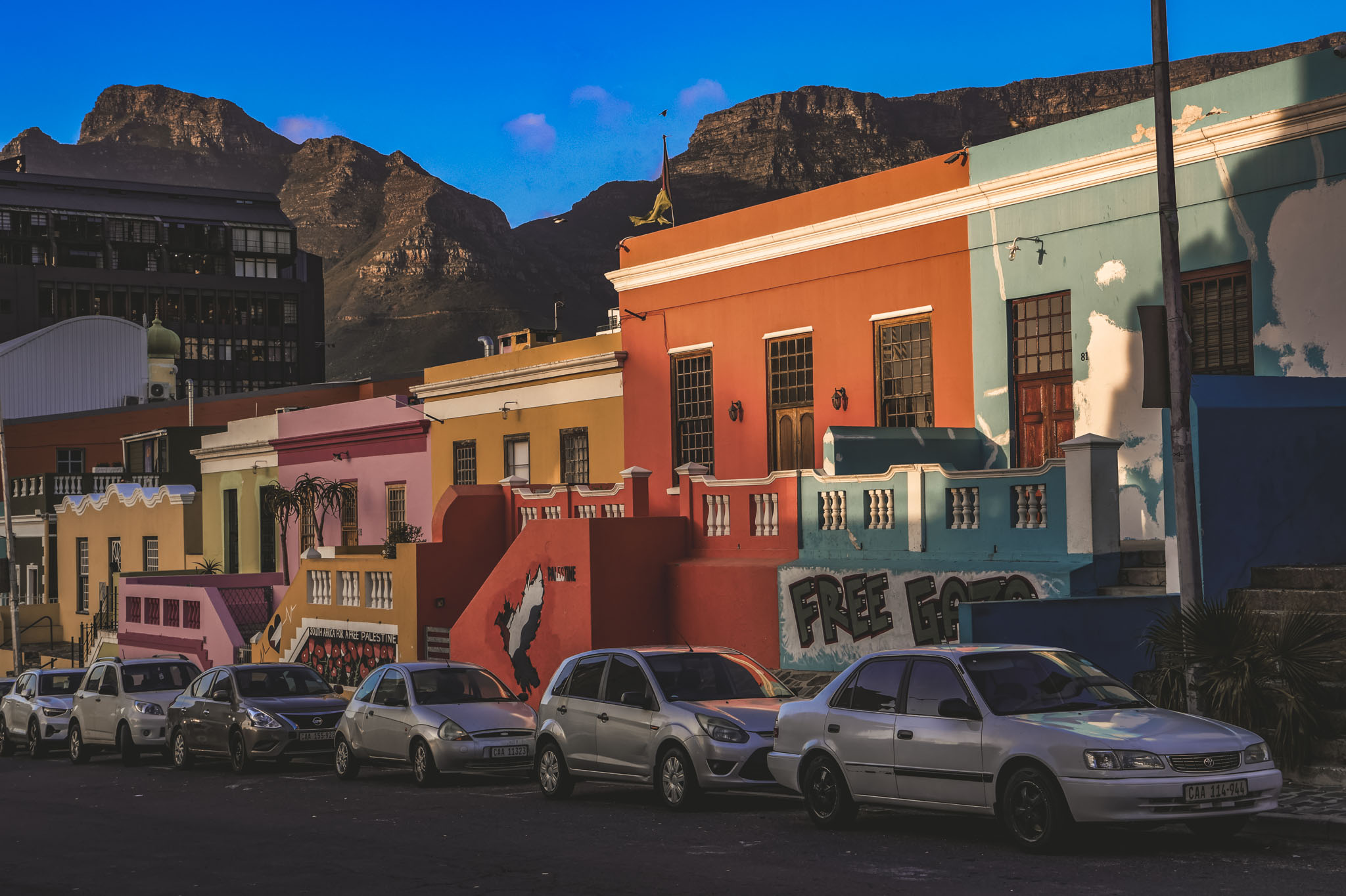 Vibrant Bo-Kaap houses in pink, orange, yellow, and turquoise with Table Mountain rising dramatically in the background under blue sky