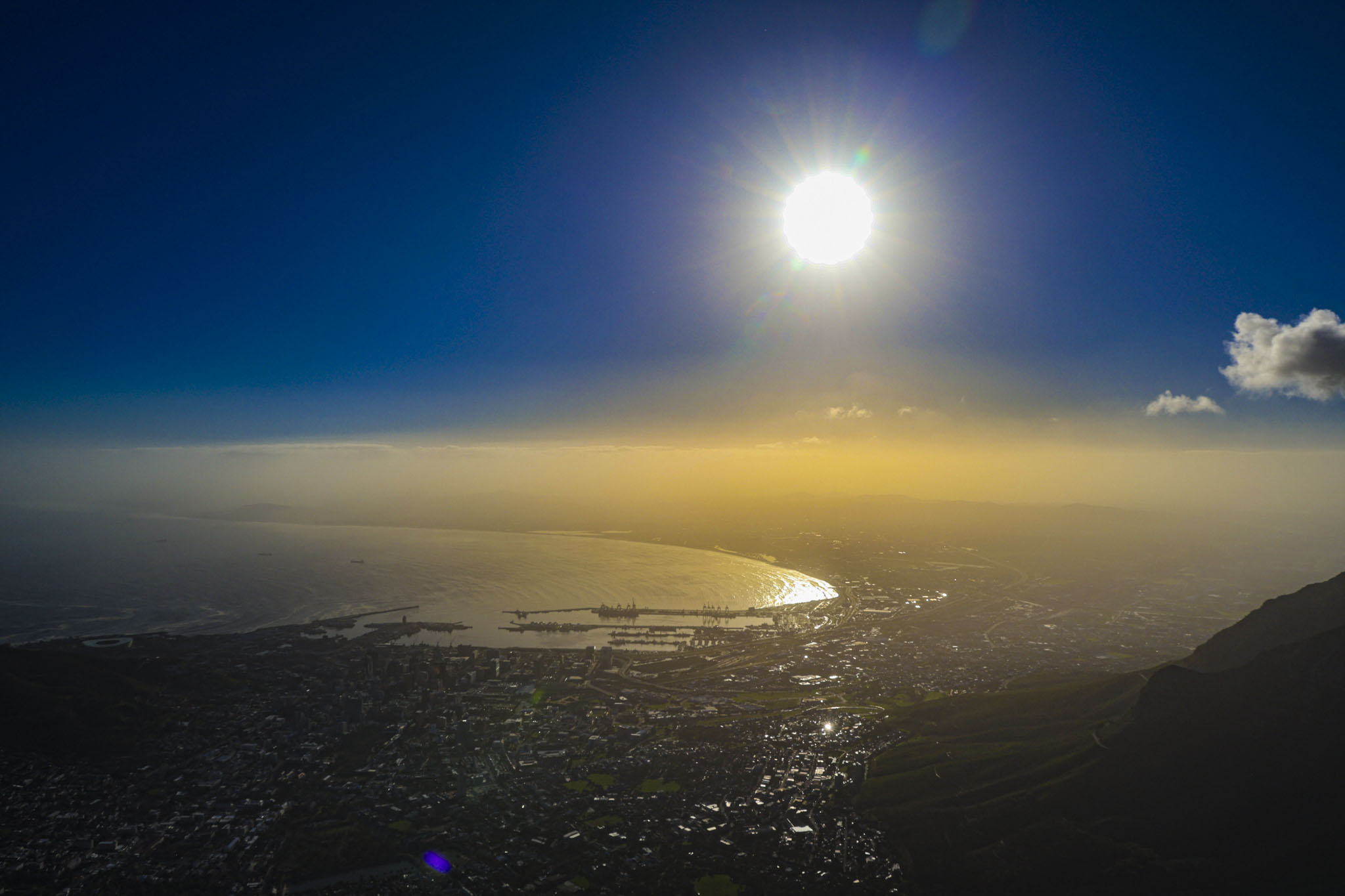 Aerial view of Cape Town and Table Bay at sunset with dramatic sunburst over the city, golden haze settling across the coastline