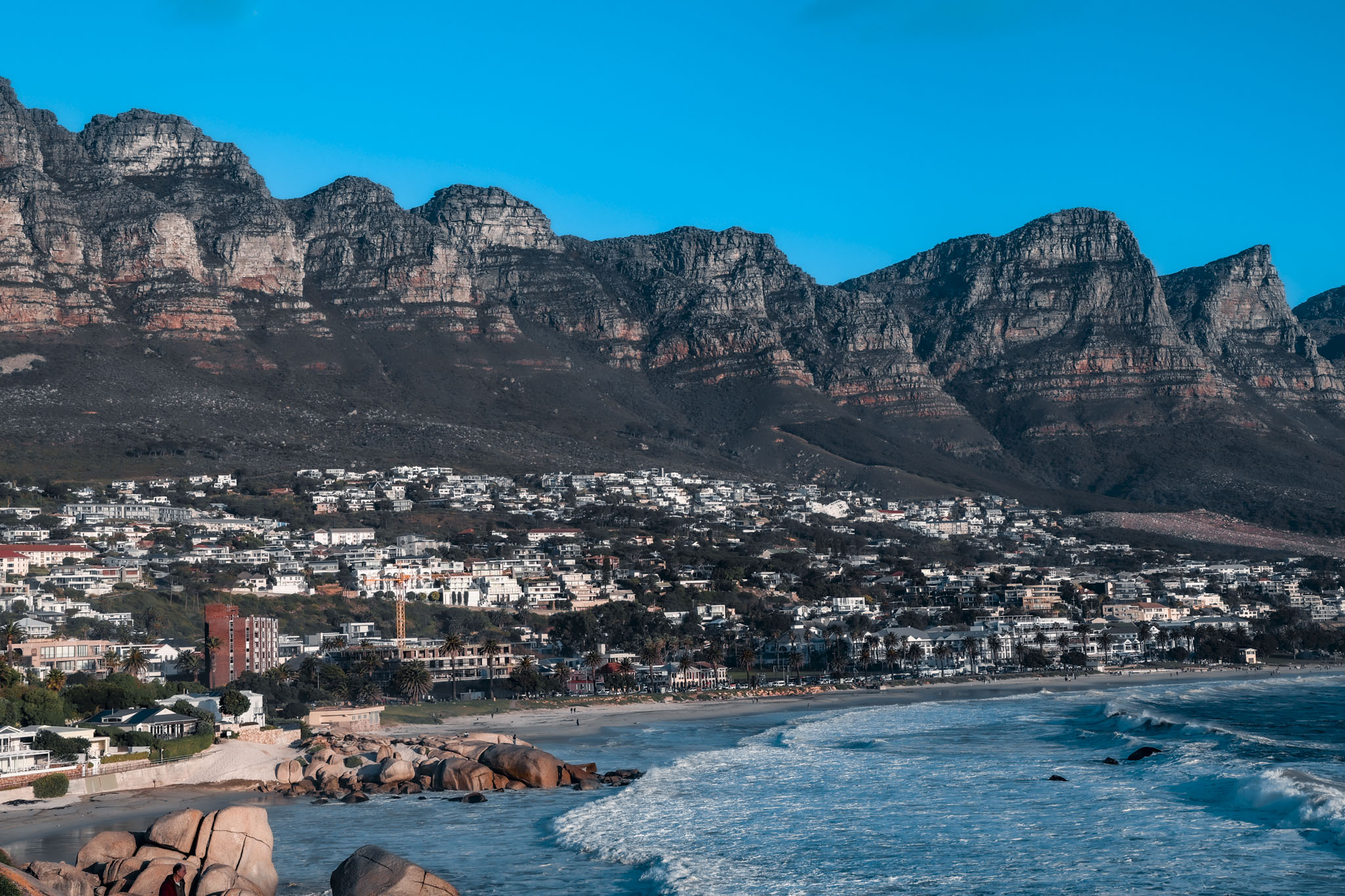 Twelve Apostles mountain range towering above Camps Bay beach with turquoise ocean and coastal homes below